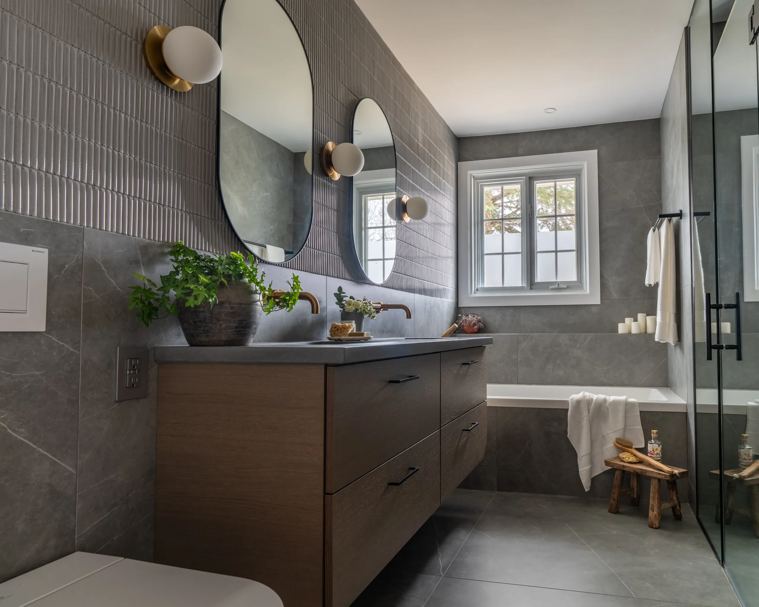 Salle de bain principale à Boucherville — vanité suspendue en noyer, robinetterie en laiton patiné, murs en micro-ciment et miroirs ovales.