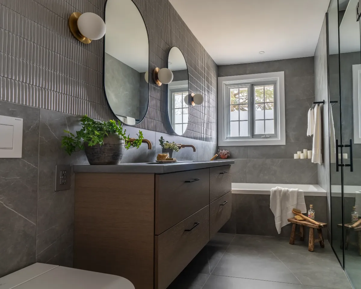Salle de bain principale à Boucherville — vanité suspendue en noyer, robinetterie en laiton patiné, murs en micro-ciment et miroirs ovales.