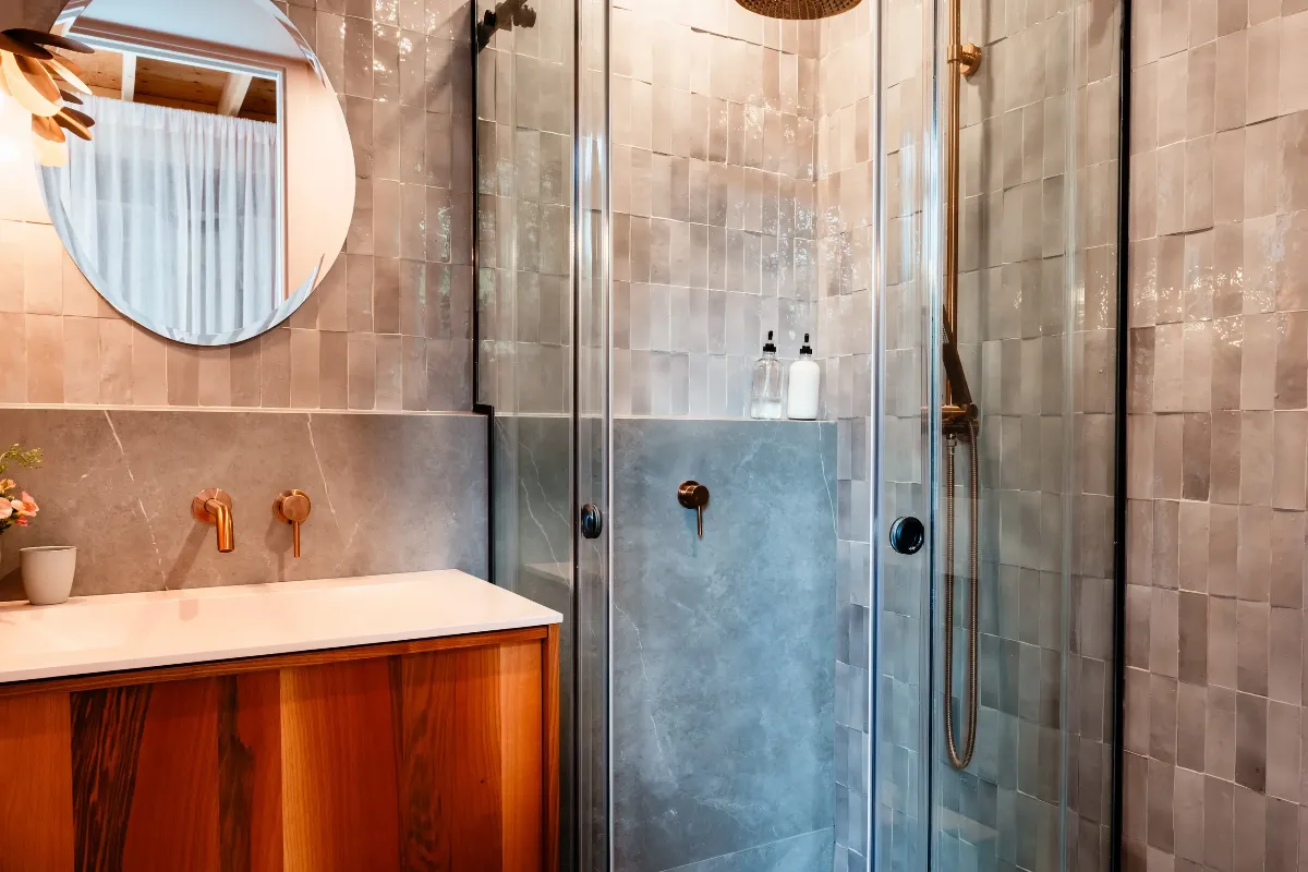 Salle de bain secondaire d'un chalet à Mont-Tremblant : douche à l'italienne avec murs de pierre naturelle et banc en bois.