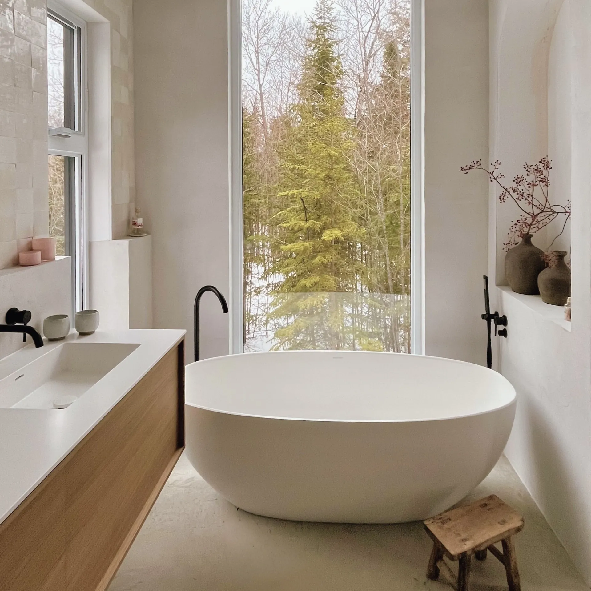 Salle de bain principale d'un chalet à Mont-Tremblant, habillée de pierre avec baignoire profonde et rideaux en lin naturel.