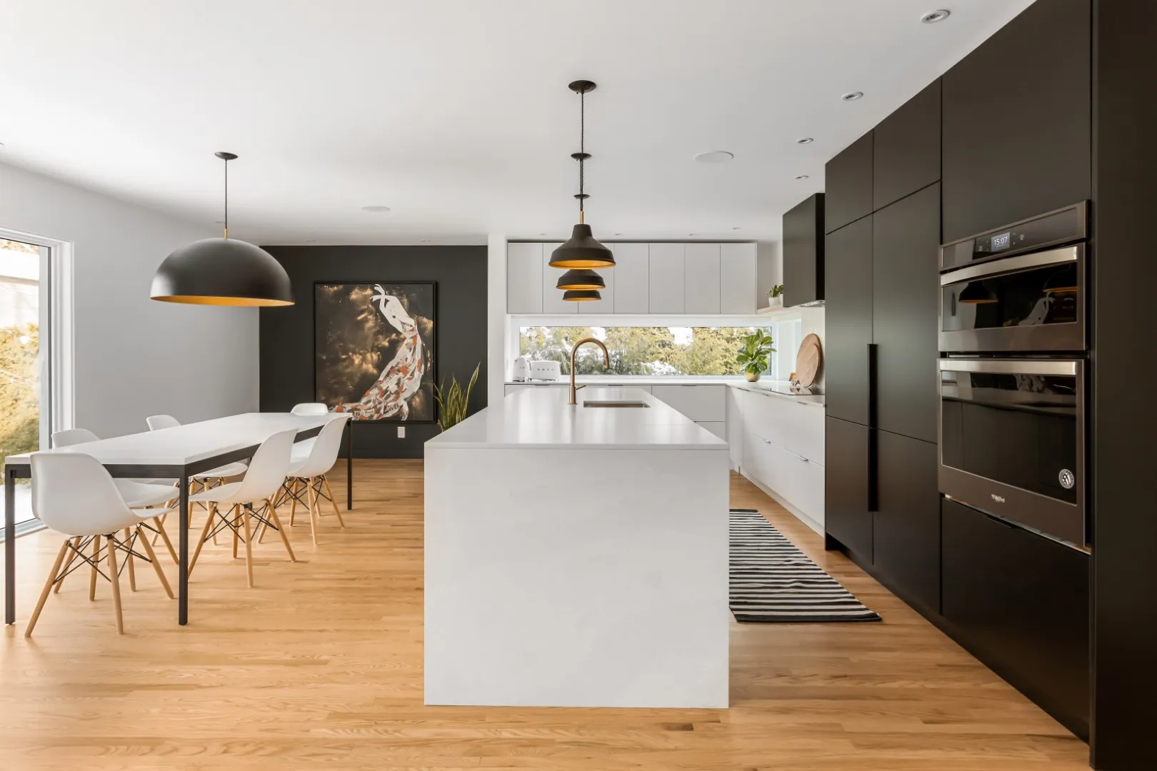 Cuisine noir et blanc avec pan de mur anthracite, suspension sculpturale en dôme et îlot en pierre pâle — bungalow de Montréal.