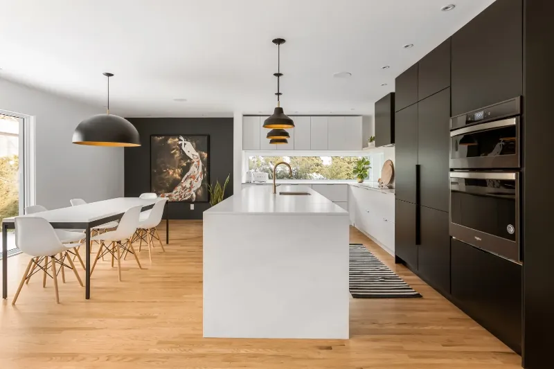 Cuisine noir et blanc avec pan de mur anthracite, suspension sculpturale en dôme et îlot en pierre pâle — bungalow de Montréal.