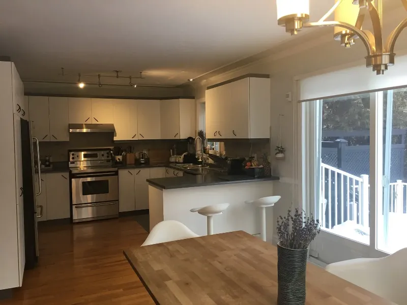 Photo avant : l'ébénisterie crème d'origine de la cuisine, les comptoirs en pierre foncée et le plan fermé — Longueuil, avant rénovation.